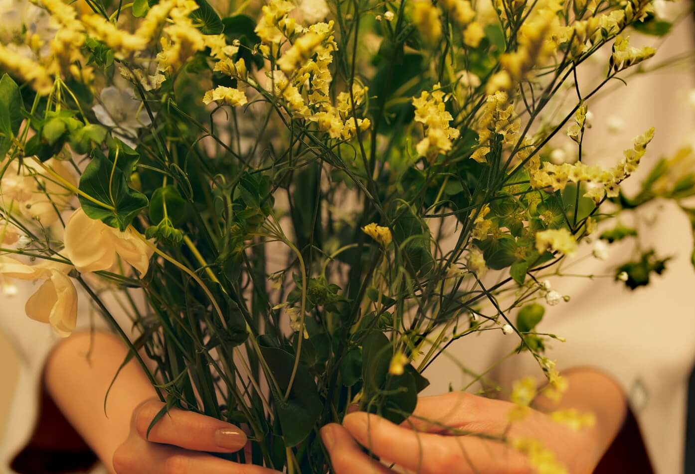 黄色い花束を大切に抱える手元。日常に彩りを添える豊かな瞬間のイメージ