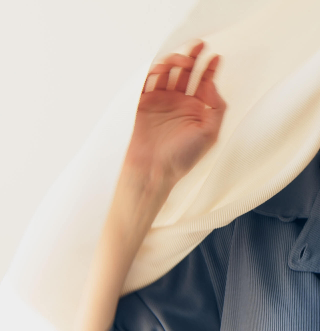 白い布越しに手を伸ばす女性。繊維と肌の触れ合いを象徴するビジュアル