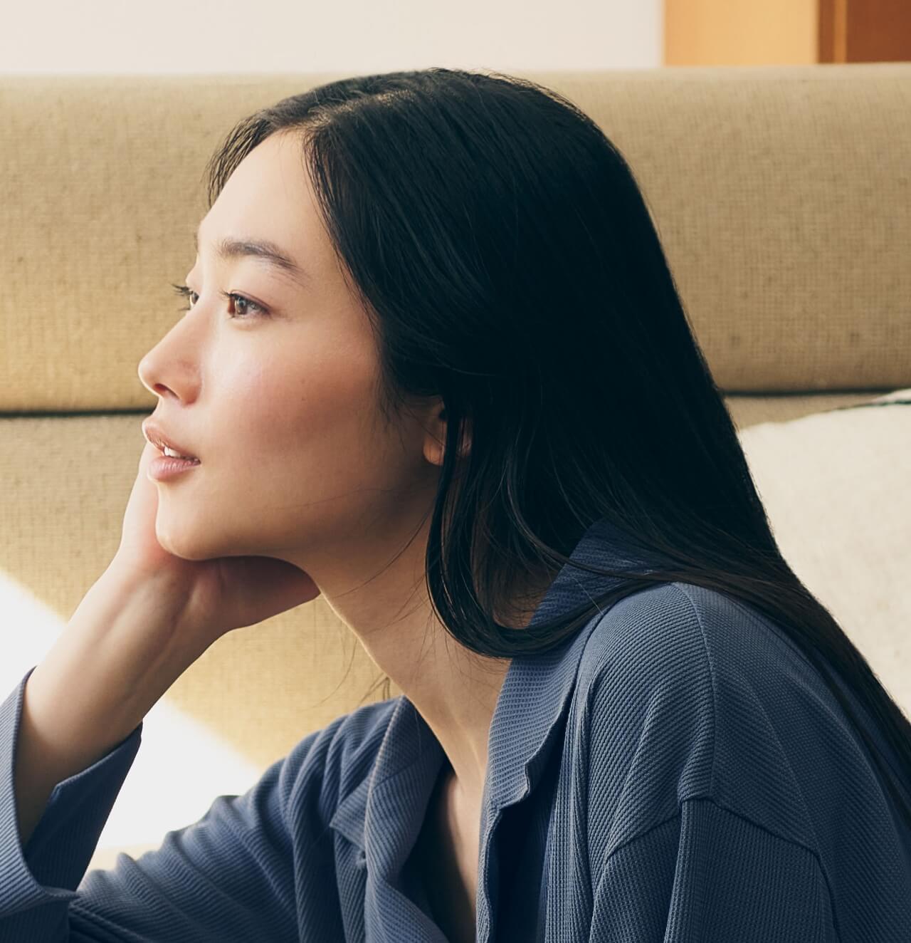 ソファで頬杖をつく女性の横顔。美容繊維がある心地よい日常のイメージ