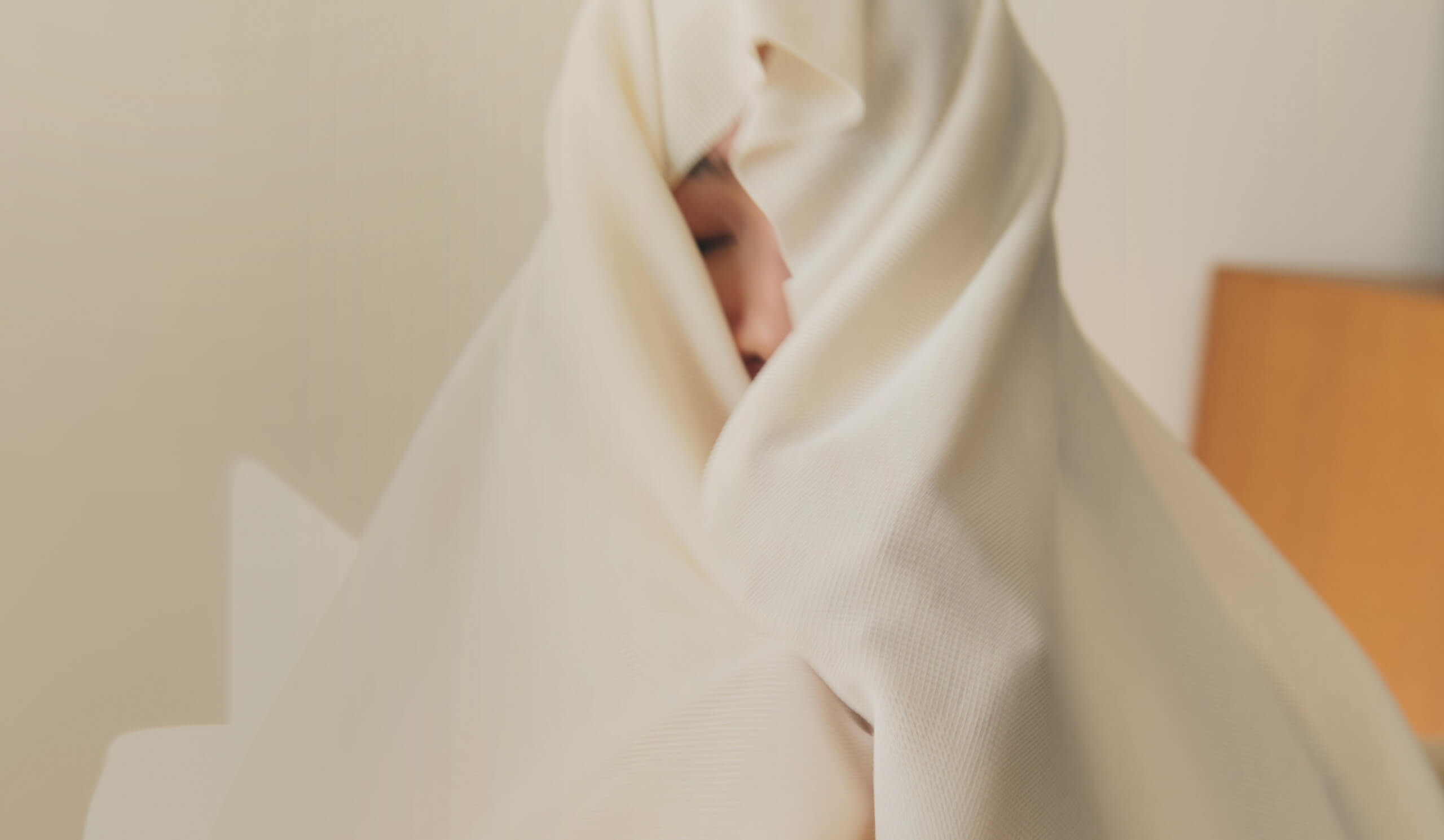 穏やかな日常と柔らかな布に包まれる女性。こころを豊かに彩る繊維の役割を象徴するイメージ